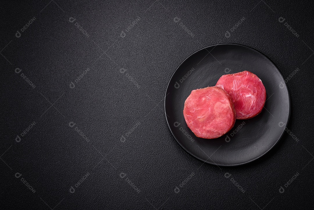 Bifes redondos de atum suculento cru com sal e especiarias sobre um fundo escuro de concreto