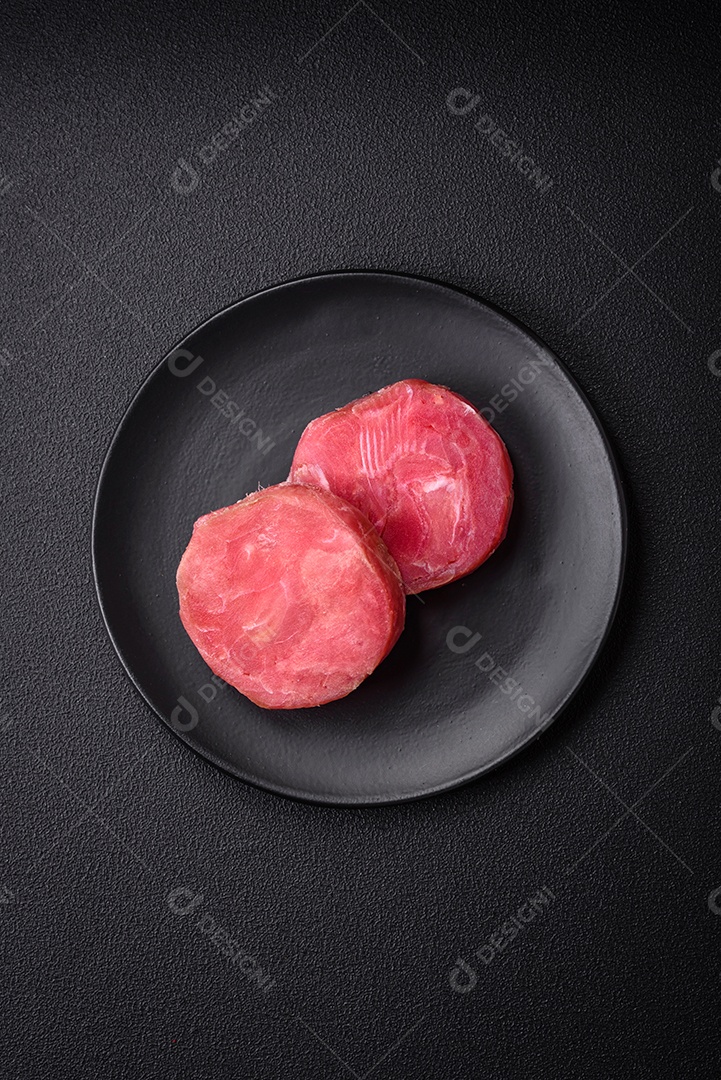 Bifes redondos de atum suculento cru com sal e especiarias sobre um fundo escuro de concreto