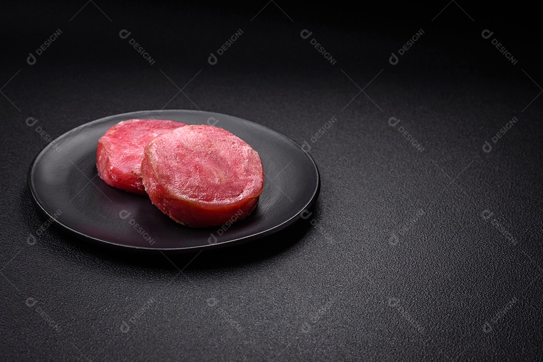 Bifes redondos de atum suculento cru com sal e especiarias sobre um fundo escuro de concreto