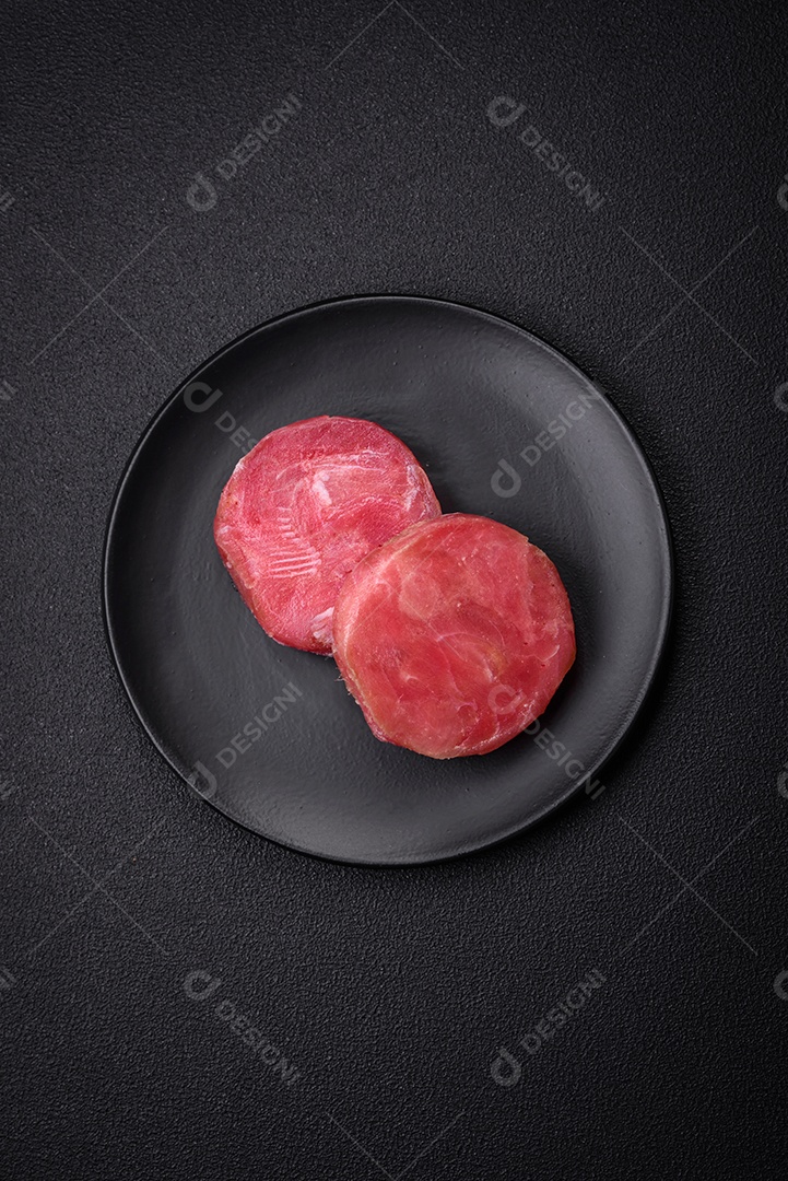 Bifes redondos de atum suculento cru com sal e especiarias sobre um fundo escuro de concreto