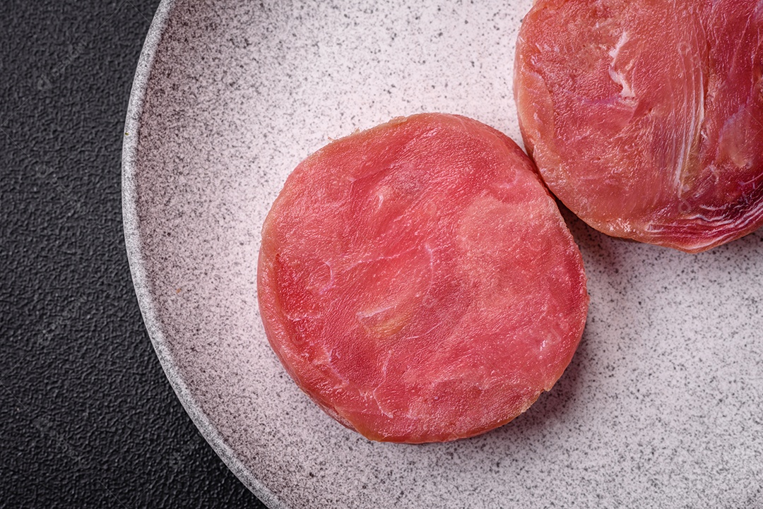 Bifes redondos de atum suculento cru com sal e especiarias sobre um fundo escuro de concreto