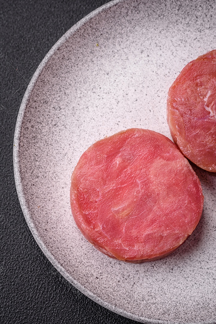 Bifes redondos de atum suculento cru com sal e especiarias sobre um fundo escuro de concreto