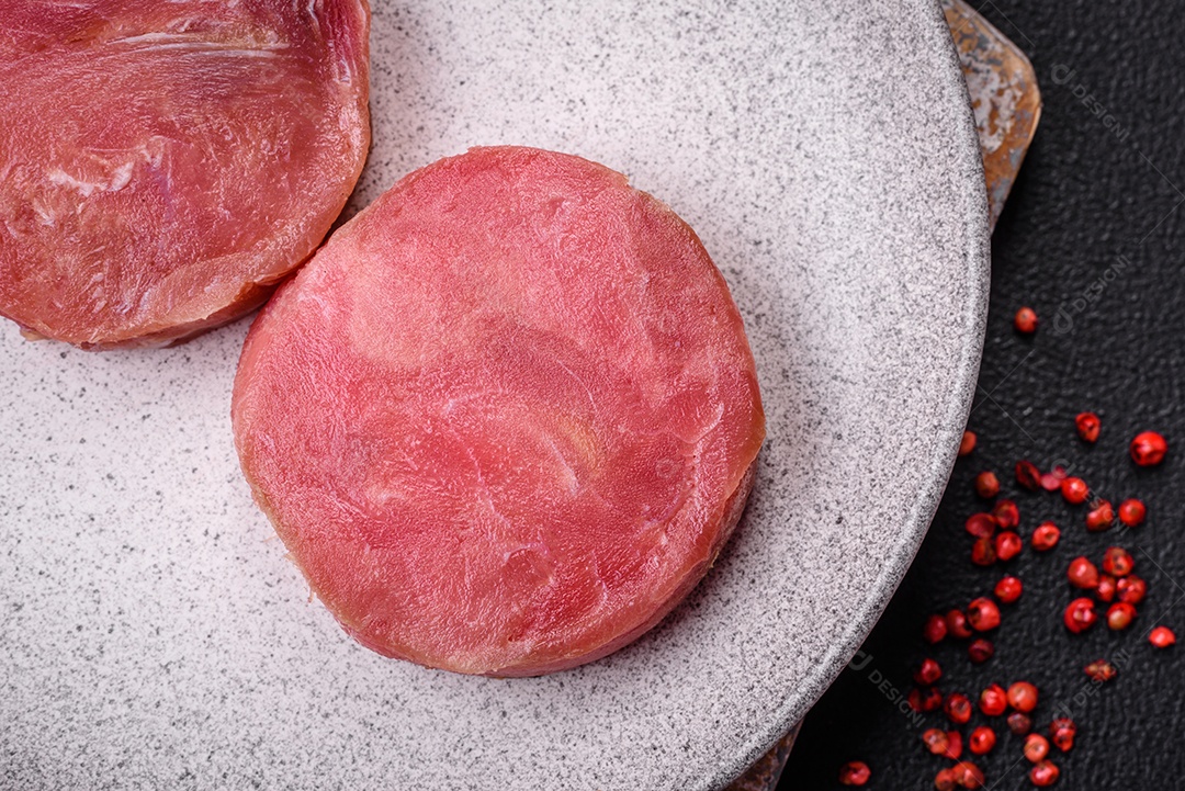 Bifes redondos de atum suculento cru com sal e especiarias sobre um fundo escuro de concreto