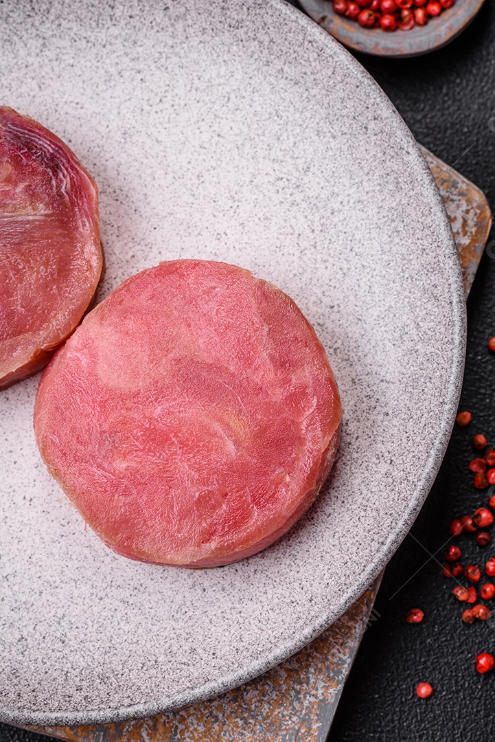 Bifes redondos de atum suculento cru com sal e especiarias sobre um fundo escuro de concreto
