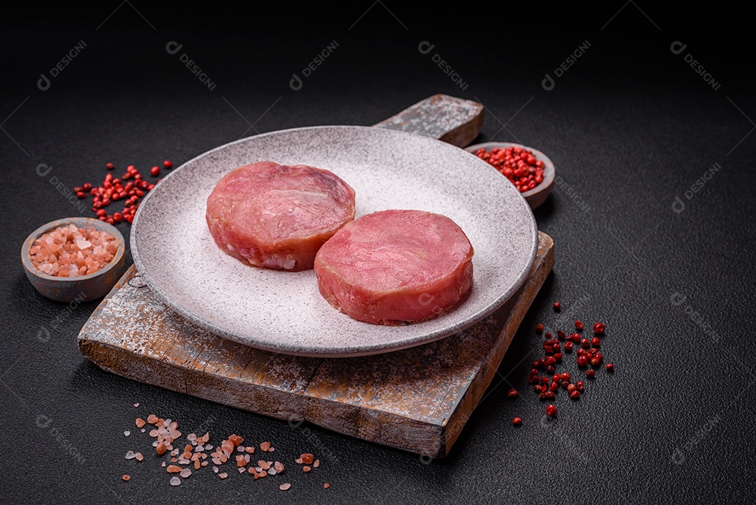 Bifes redondos de atum suculento cru com sal e especiarias sobre um fundo escuro de concreto