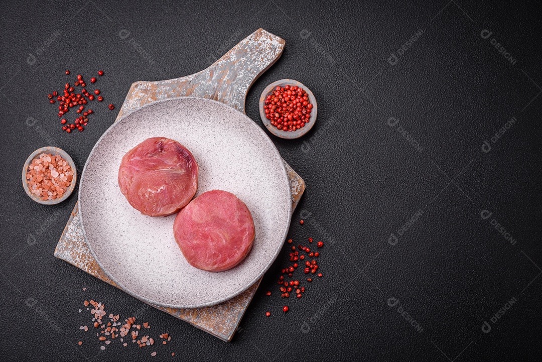 Bifes redondos de atum suculento cru com sal e especiarias sobre um fundo escuro de concreto