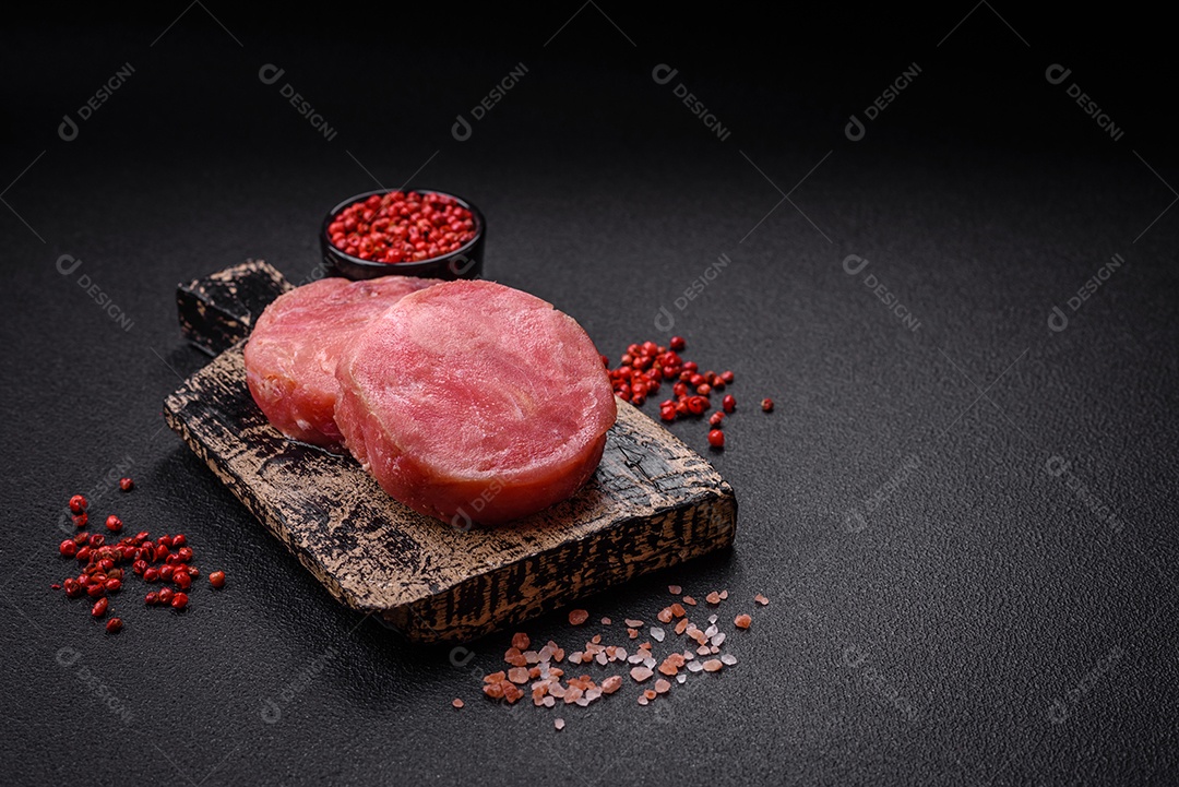 Bifes redondos de atum suculento cru com sal e especiarias sobre um fundo escuro de concreto