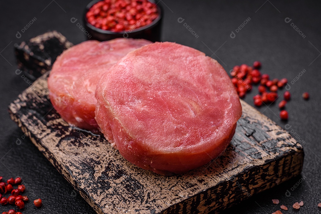 Bifes redondos de atum suculento cru com sal e especiarias sobre um fundo escuro de concreto