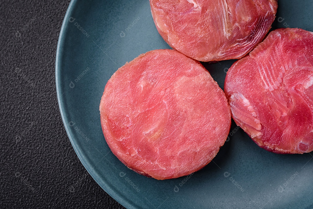 Bifes redondos de atum suculento cru com sal e especiarias sobre um fundo escuro de concreto