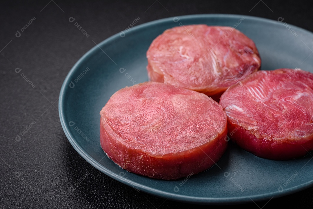 Bifes redondos de atum suculento cru com sal e especiarias sobre um fundo escuro de concreto