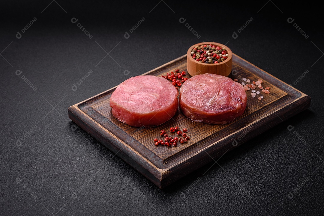 Bifes redondos de atum suculento cru com sal e especiarias sobre um fundo escuro de concreto