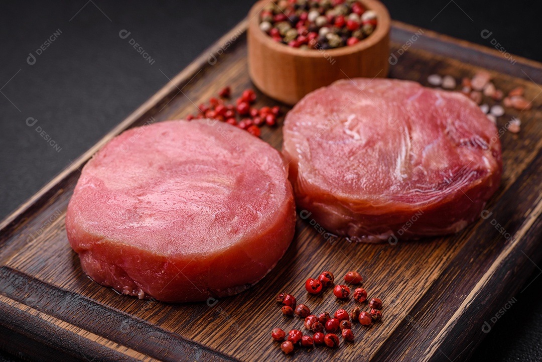 Bifes redondos de atum suculento cru com sal e especiarias sobre um fundo escuro de concreto