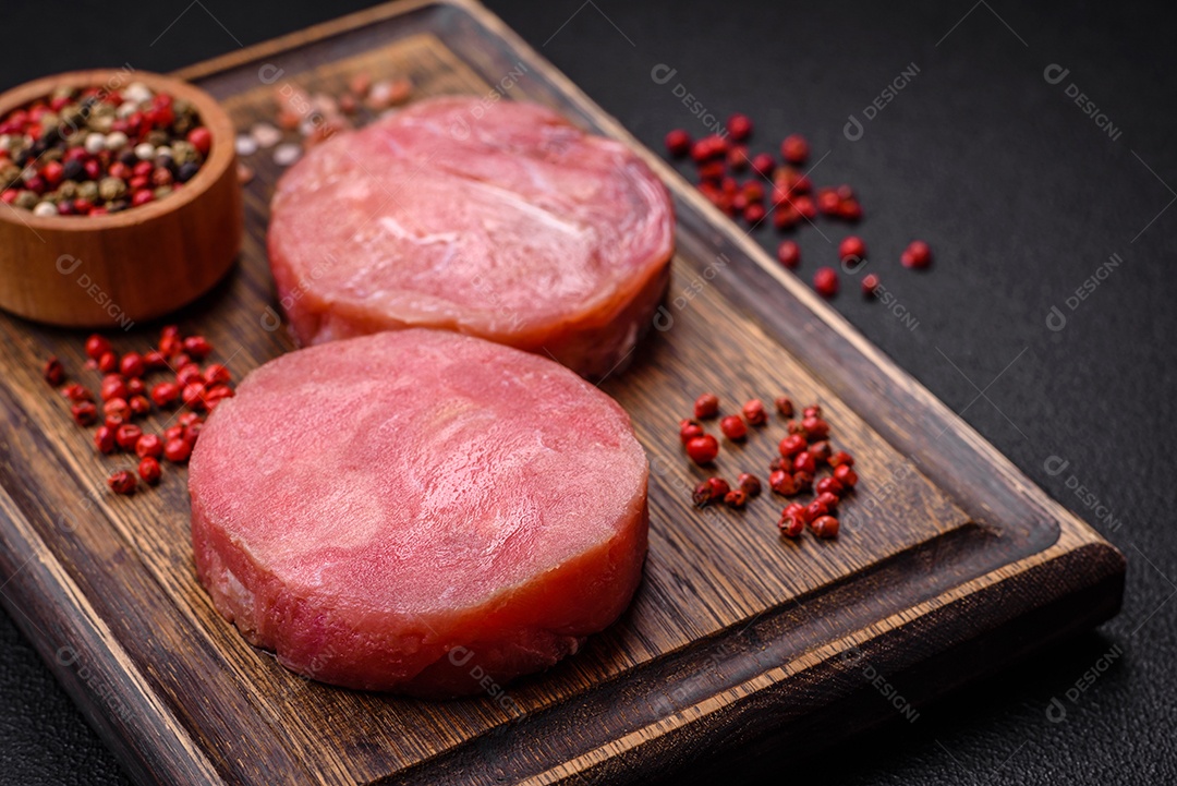 Bifes redondos de atum suculento cru com sal e especiarias sobre um fundo escuro de concreto