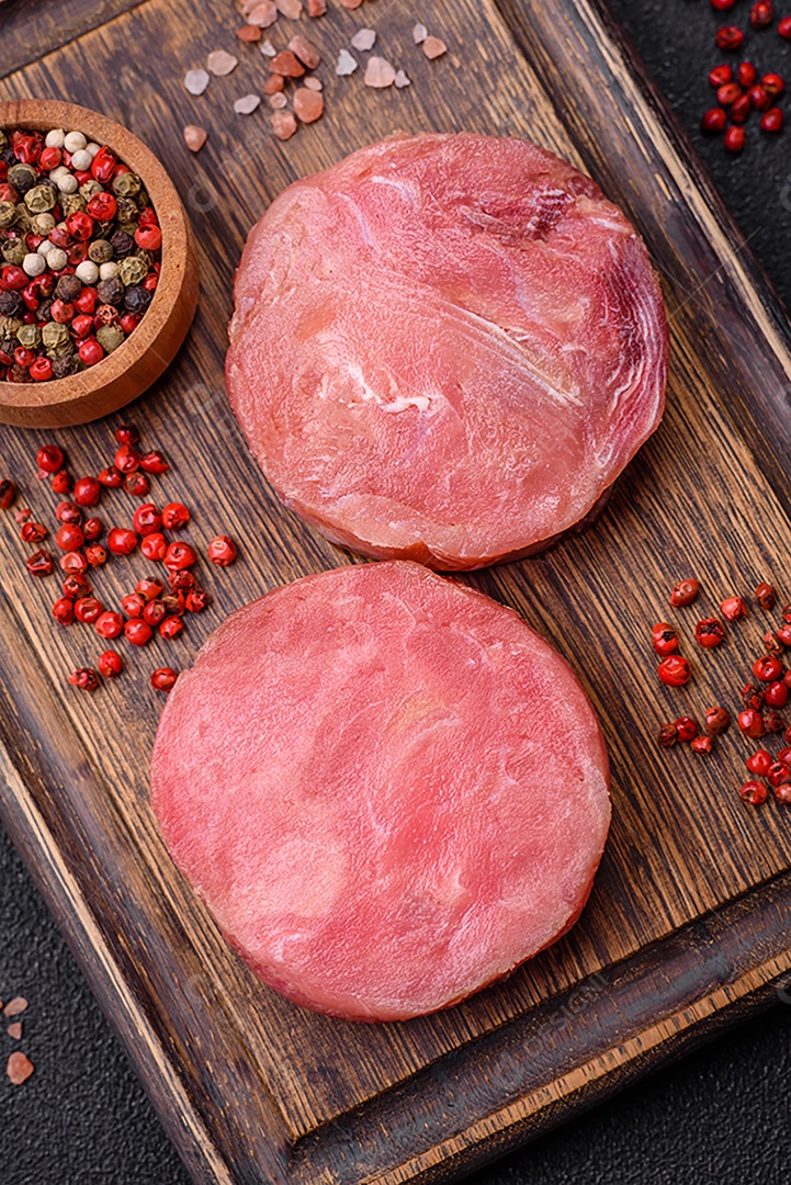 Bifes redondos de atum suculento cru com sal e especiarias sobre um fundo escuro de concreto