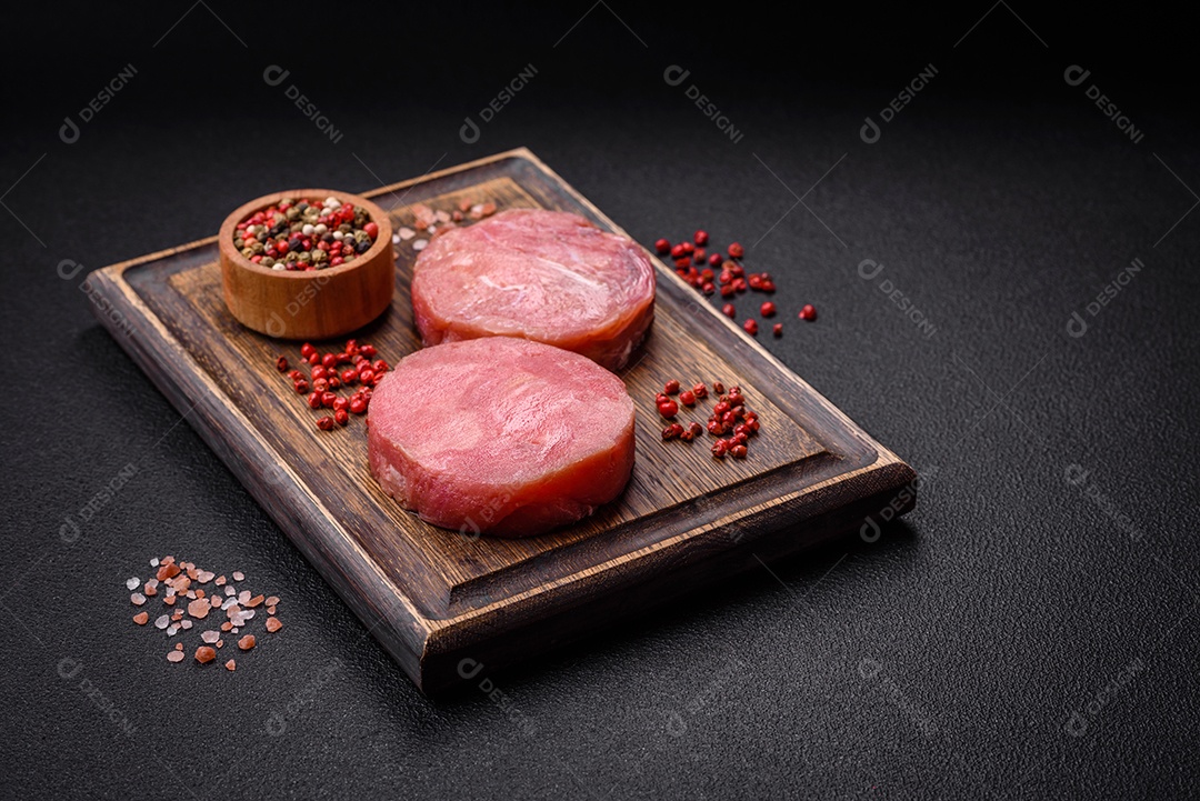 Bifes redondos de atum suculento cru com sal e especiarias sobre um fundo escuro de concreto