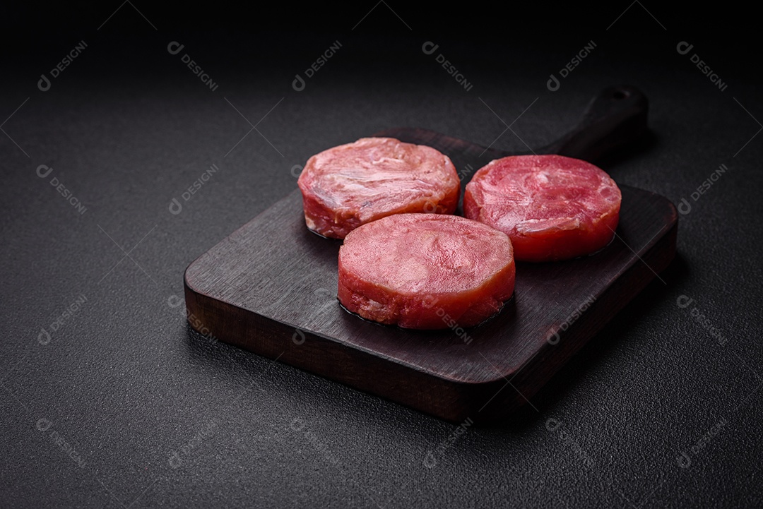 Bifes redondos de atum suculento cru com sal e especiarias sobre um fundo escuro de concreto