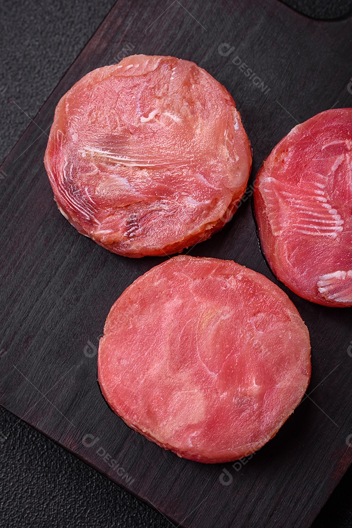 Bifes redondos de atum suculento cru com sal e especiarias sobre um fundo escuro de concreto