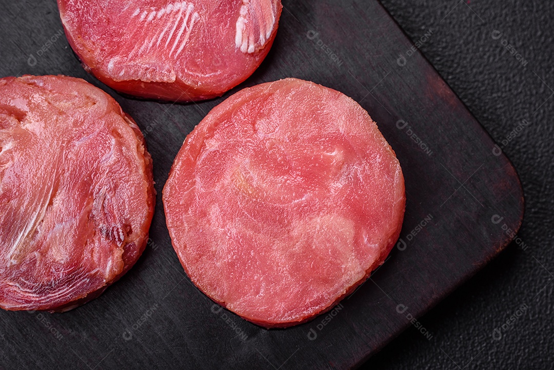 Bifes redondos de atum suculento cru com sal e especiarias sobre um fundo escuro de concreto
