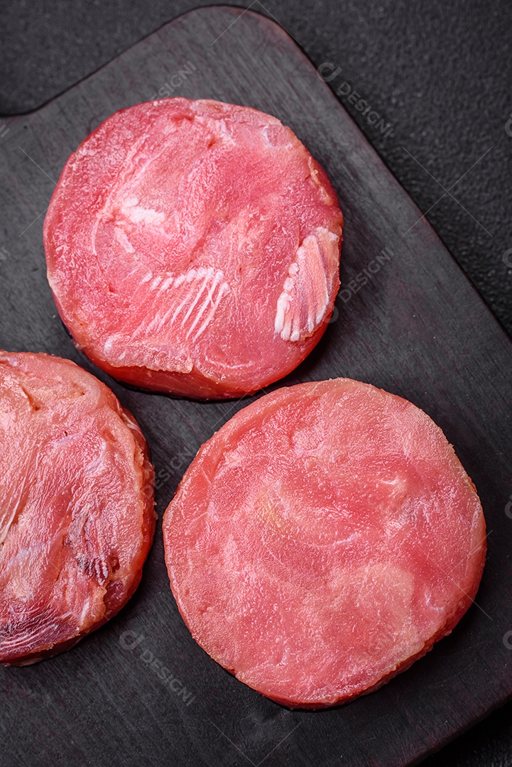 Bifes redondos de atum suculento cru com sal e especiarias sobre um fundo escuro de concreto