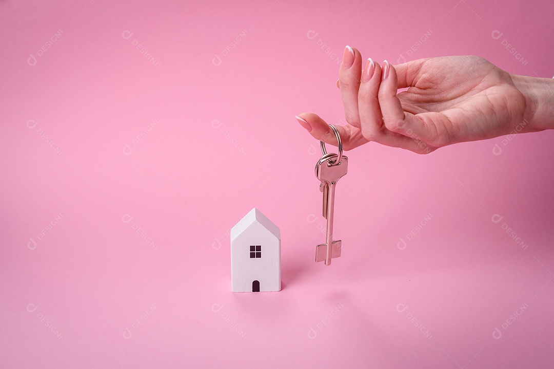 Mãos pessoa, uma casinha de madeira e chaves como ideia para investir na casa própria e atingir o objetivo de comprar um imóvel. Plano de fundo para sua ideia
