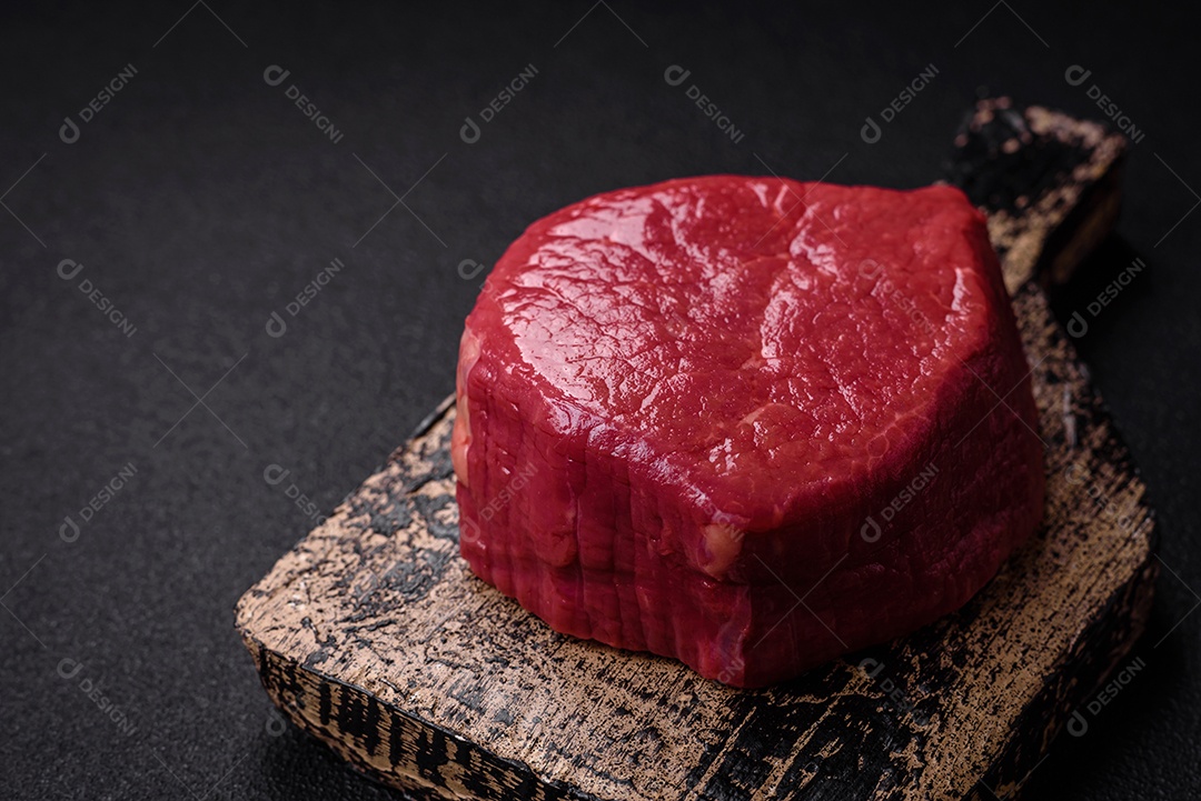 Carne crua fresca e suculenta com sal, especiarias e ervas sobre um fundo de concreto texturizado escuro