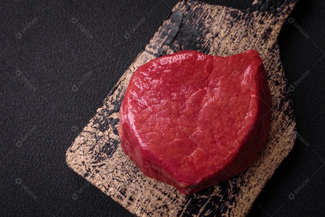 Carne crua fresca e suculenta com sal, especiarias e ervas sobre um fundo de concreto texturizado escuro