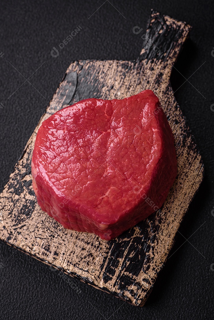 Carne crua fresca e suculenta com sal, especiarias e ervas sobre um fundo de concreto texturizado escuro