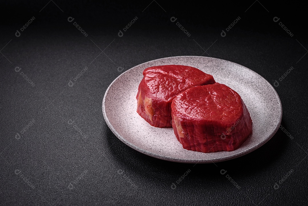 Carne crua fresca e suculenta com sal, especiarias e ervas sobre um fundo de concreto texturizado escuro