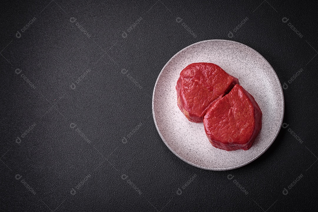 Carne crua fresca e suculenta com sal, especiarias e ervas sobre um fundo de concreto texturizado escuro