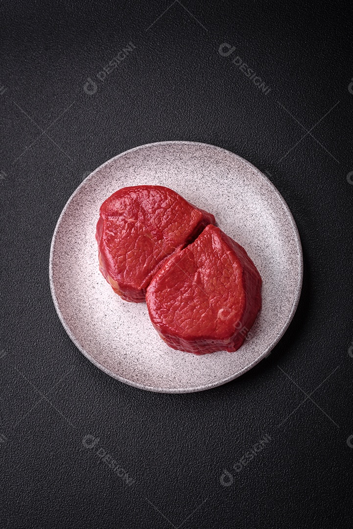 Carne crua fresca e suculenta com sal, especiarias e ervas sobre um fundo de concreto texturizado escuro