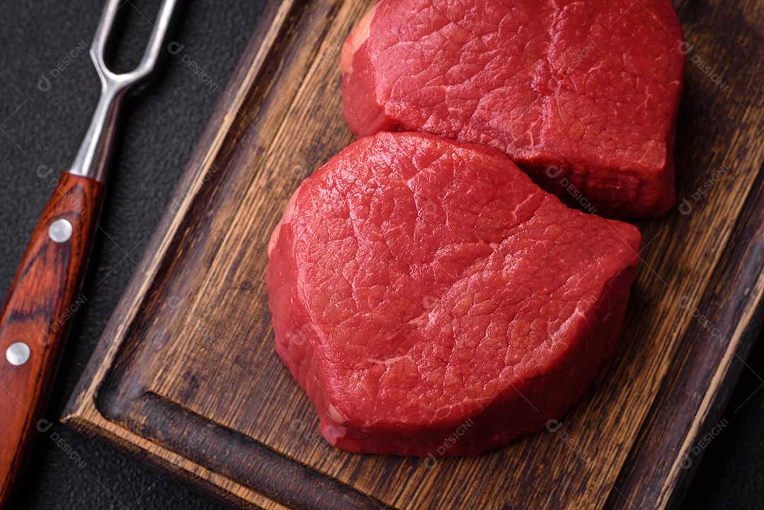 Carne crua fresca e suculenta com sal, especiarias e ervas sobre um fundo de concreto texturizado escuro