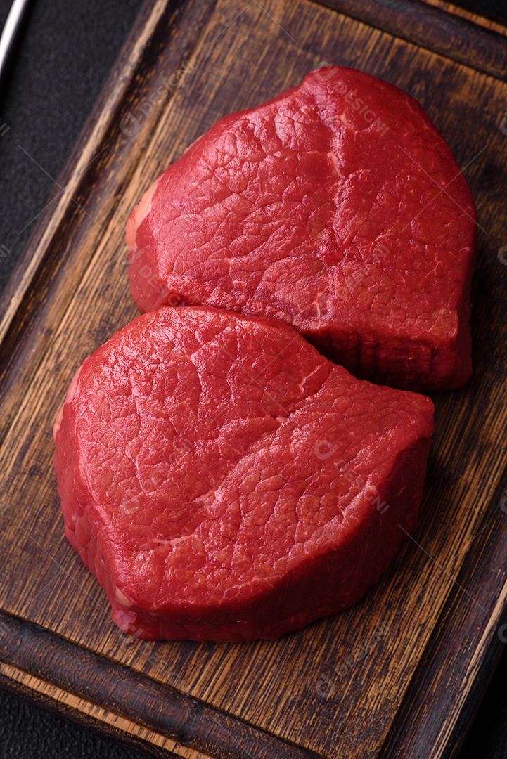 Carne crua fresca e suculenta com sal, especiarias e ervas sobre um fundo de concreto texturizado escuro