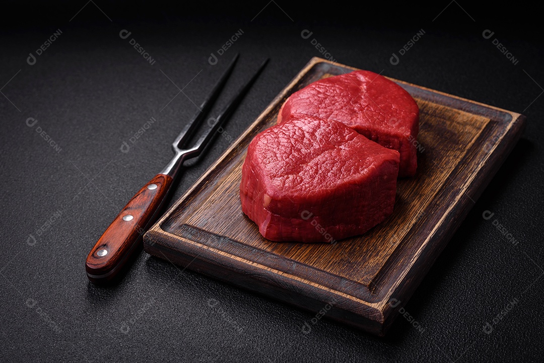 Carne crua fresca e suculenta com sal, especiarias e ervas sobre um fundo de concreto texturizado escuro