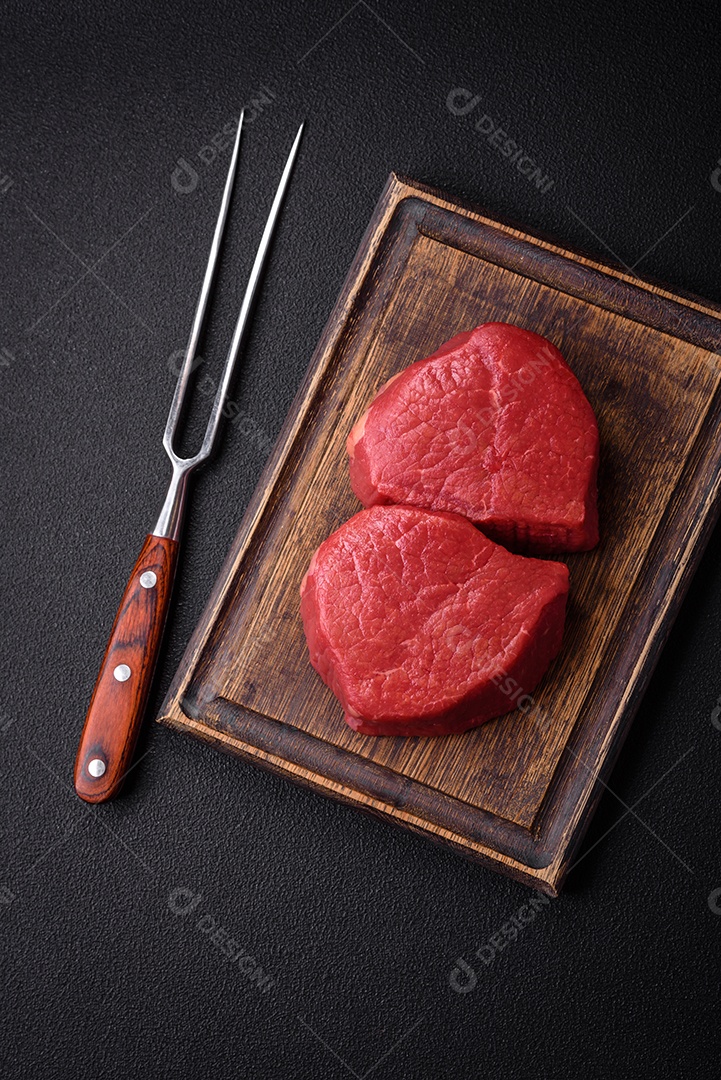 Carne crua fresca e suculenta com sal, especiarias e ervas sobre um fundo de concreto texturizado escuro