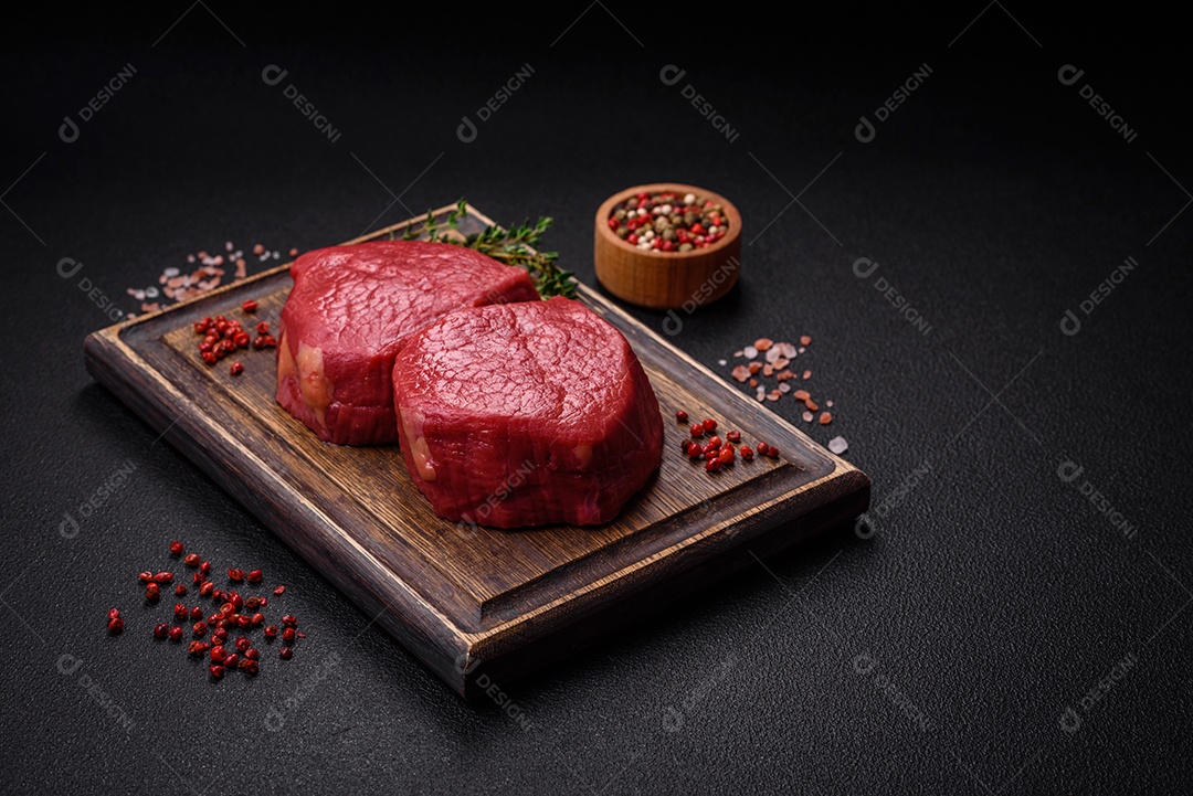 Carne crua fresca e suculenta com sal, especiarias e ervas sobre um fundo de concreto texturizado escuro