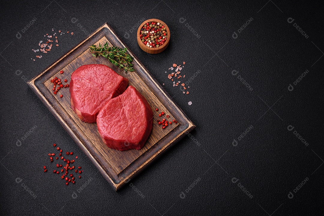 Carne crua fresca e suculenta com sal, especiarias e ervas sobre um fundo de concreto texturizado escuro