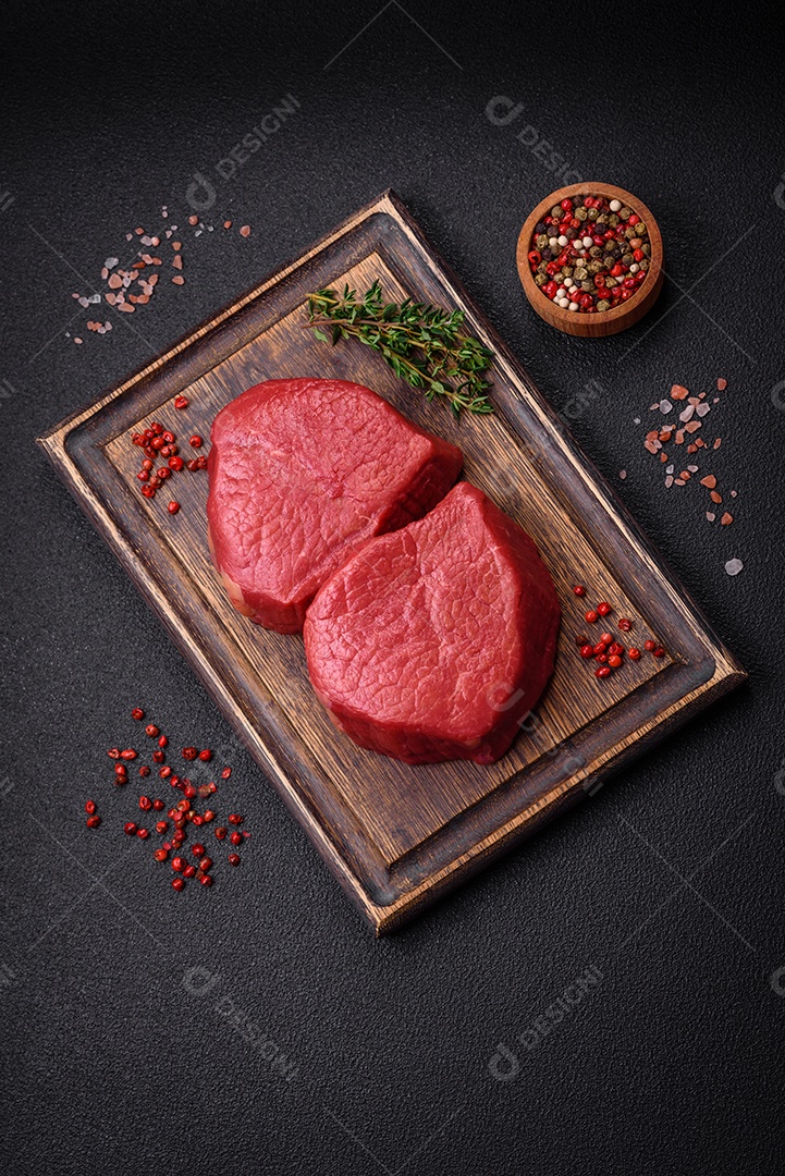 Carne crua fresca e suculenta com sal, especiarias e ervas sobre um fundo de concreto texturizado escuro