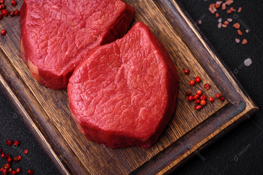 Carne crua fresca e suculenta com sal, especiarias e ervas sobre um fundo de concreto texturizado escuro