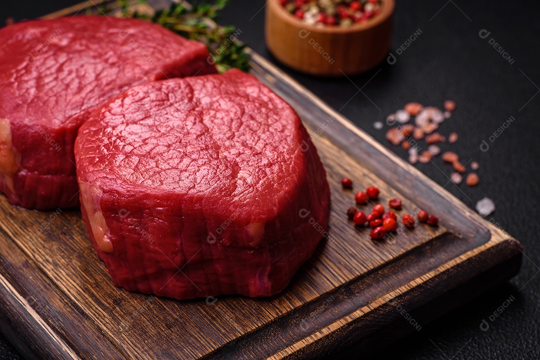 Carne crua fresca e suculenta com sal, especiarias e ervas sobre um fundo de concreto texturizado escuro