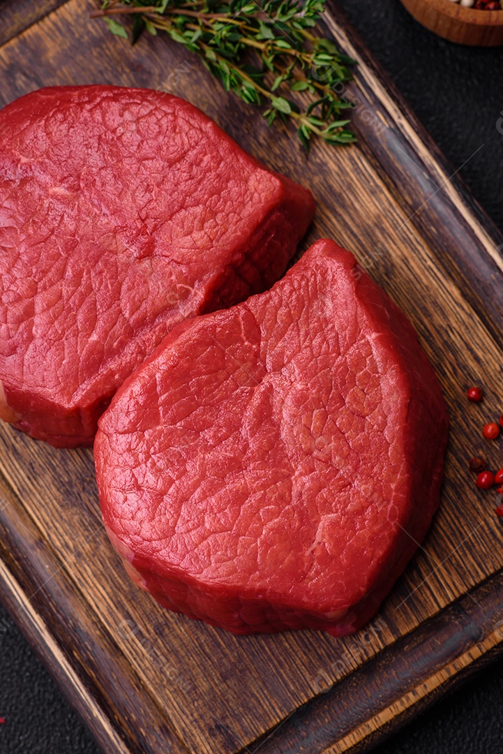 Carne crua fresca e suculenta com sal, especiarias e ervas sobre um fundo de concreto texturizado escuro