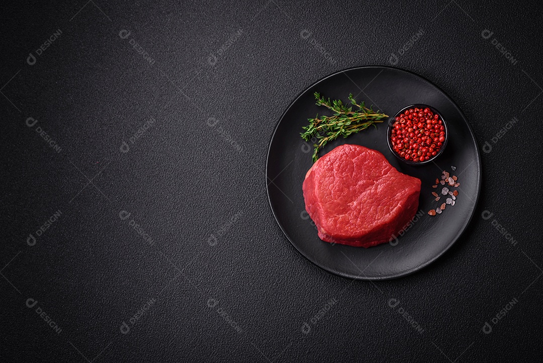 Carne crua fresca e suculenta com sal, especiarias e ervas sobre um fundo de concreto texturizado escuro