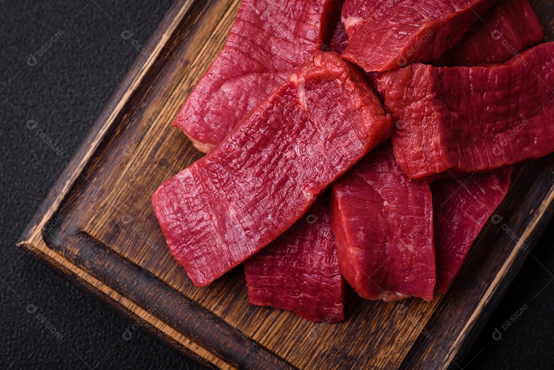 Carne crua fresca e suculenta com sal, especiarias e ervas sobre um fundo de concreto texturizado escuro