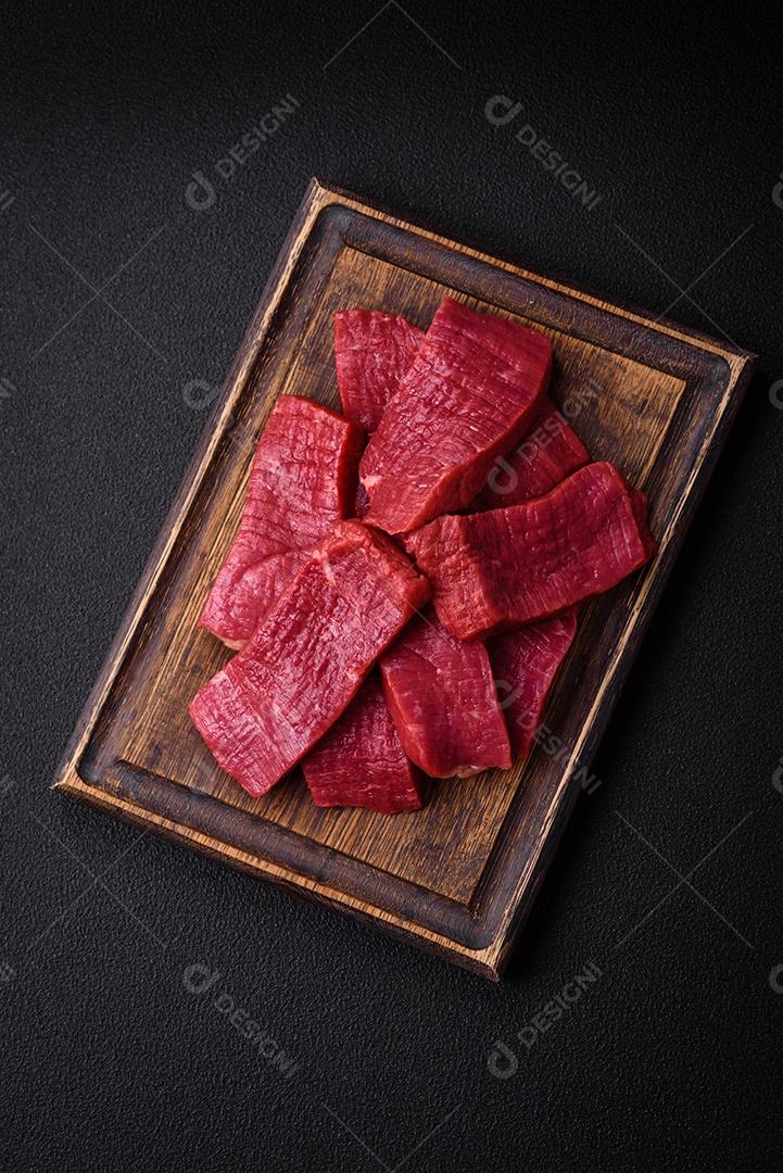 Carne crua fresca e suculenta com sal, especiarias e ervas sobre um fundo de concreto texturizado escuro