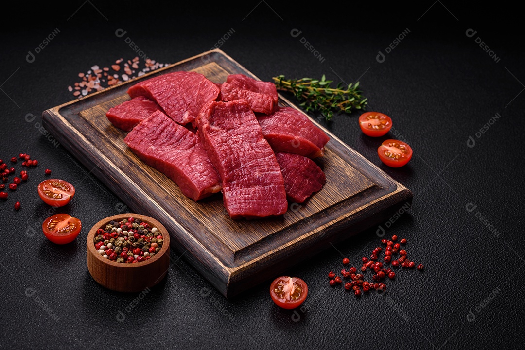 Carne crua fresca e suculenta com sal, especiarias e ervas sobre um fundo de concreto texturizado escuro