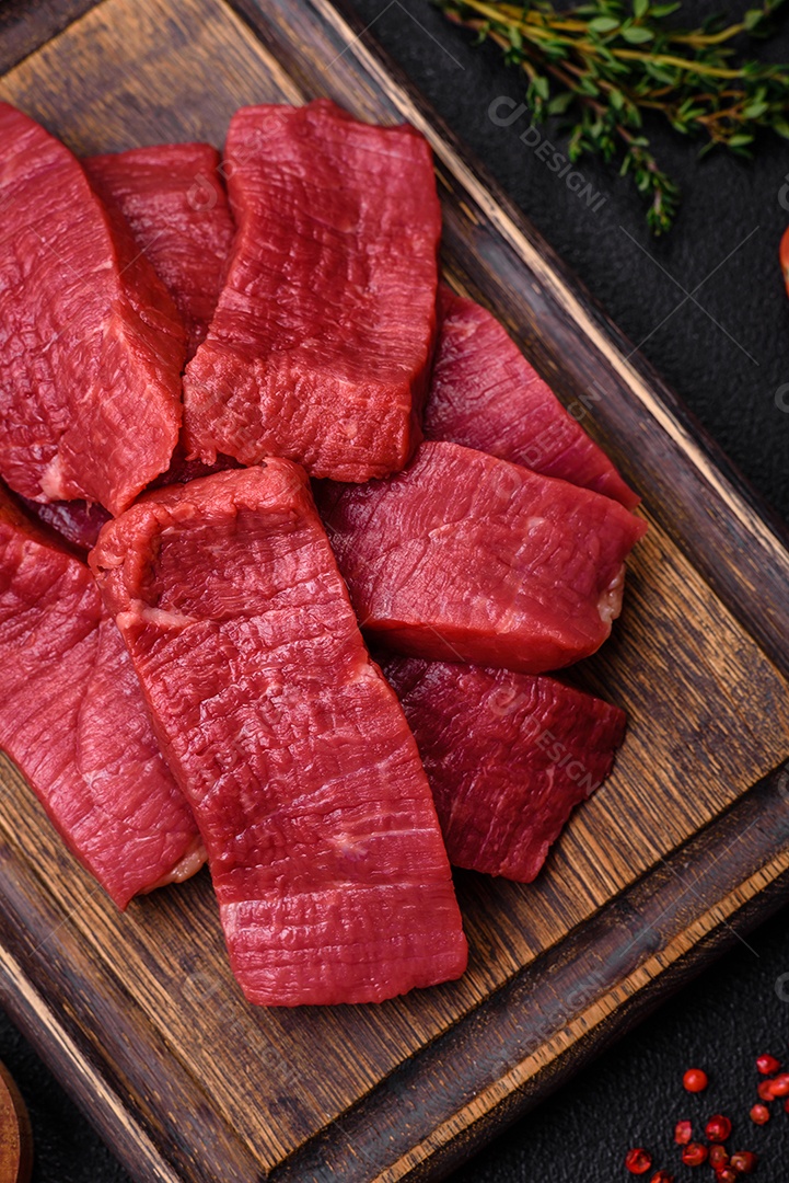 Carne crua fresca e suculenta com sal, especiarias e ervas sobre um fundo de concreto texturizado escuro