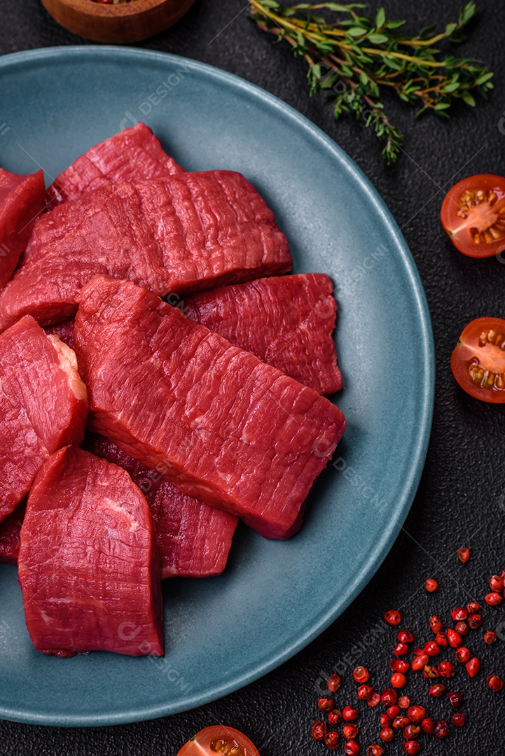 Carne crua fresca e suculenta com sal, especiarias e ervas sobre um fundo de concreto texturizado escuro