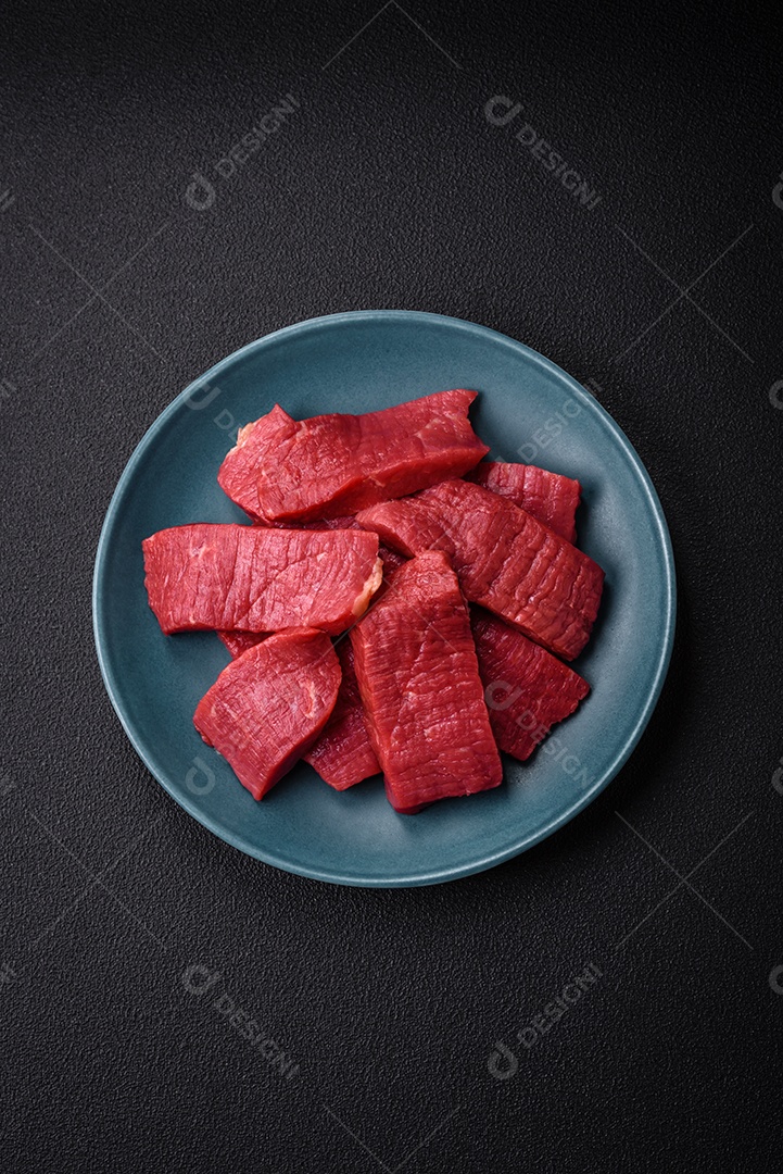 Carne crua fresca e suculenta com sal, especiarias e ervas sobre um fundo de concreto texturizado escuro