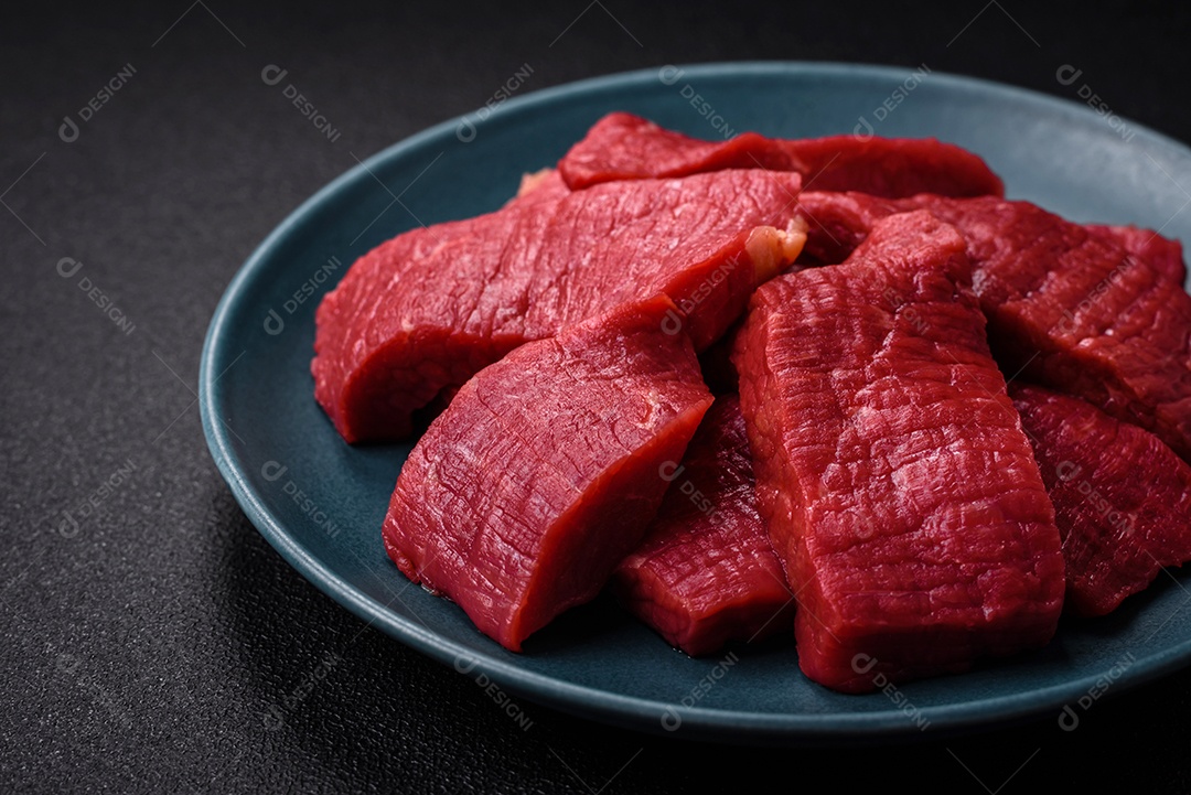 Carne crua fresca e suculenta com sal, especiarias e ervas sobre um fundo de concreto texturizado escuro