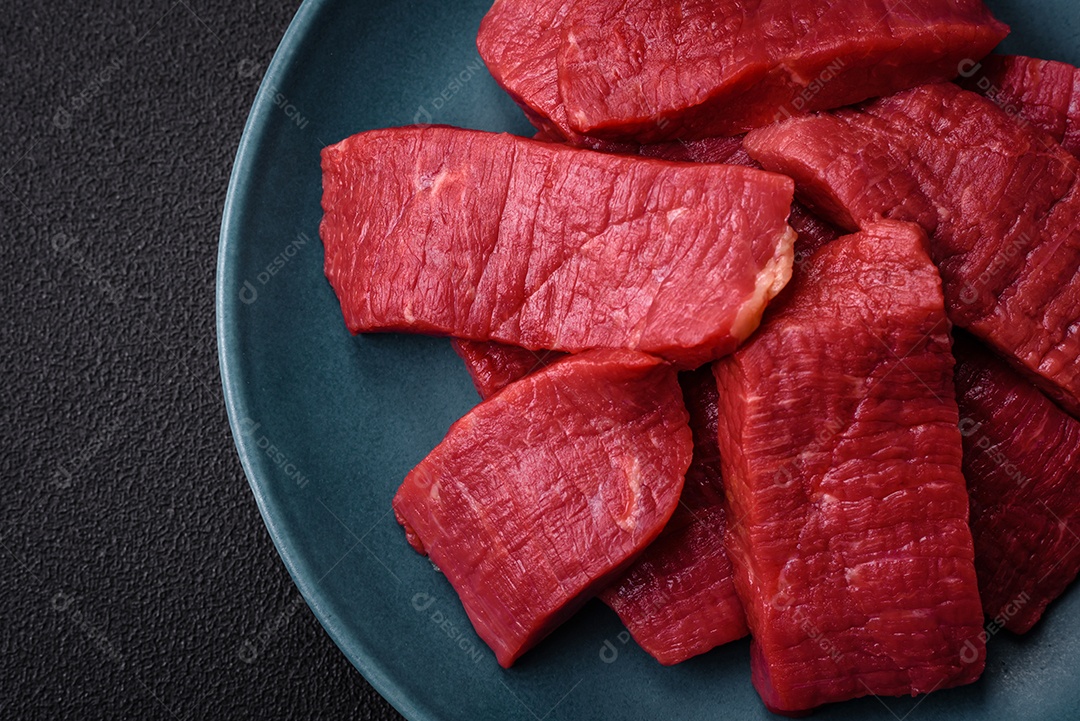 Carne crua fresca e suculenta com sal, especiarias e ervas sobre um fundo de concreto texturizado escuro