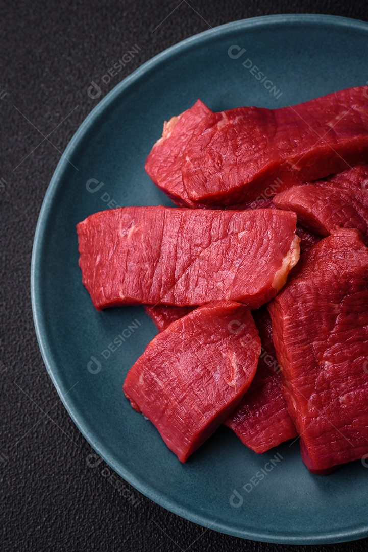 Carne crua fresca e suculenta com sal, especiarias e ervas sobre um fundo de concreto texturizado escuro